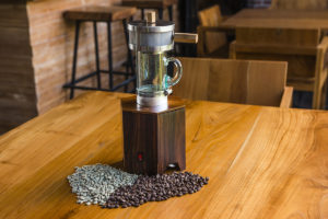 Pictured is a Power Roaster on a table with fresh beans on left and roasted beans on right.